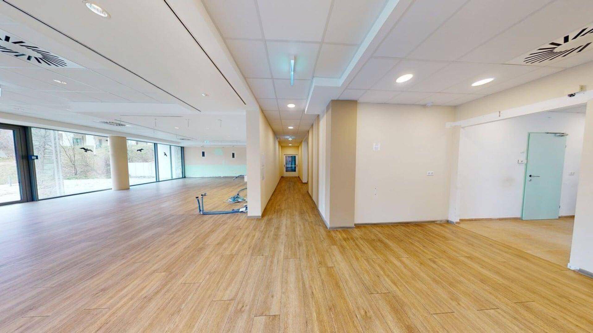 Langer Flur in einem Gewerberaum mit Holzboden, der zu einem großen, hellen Bereich führt.