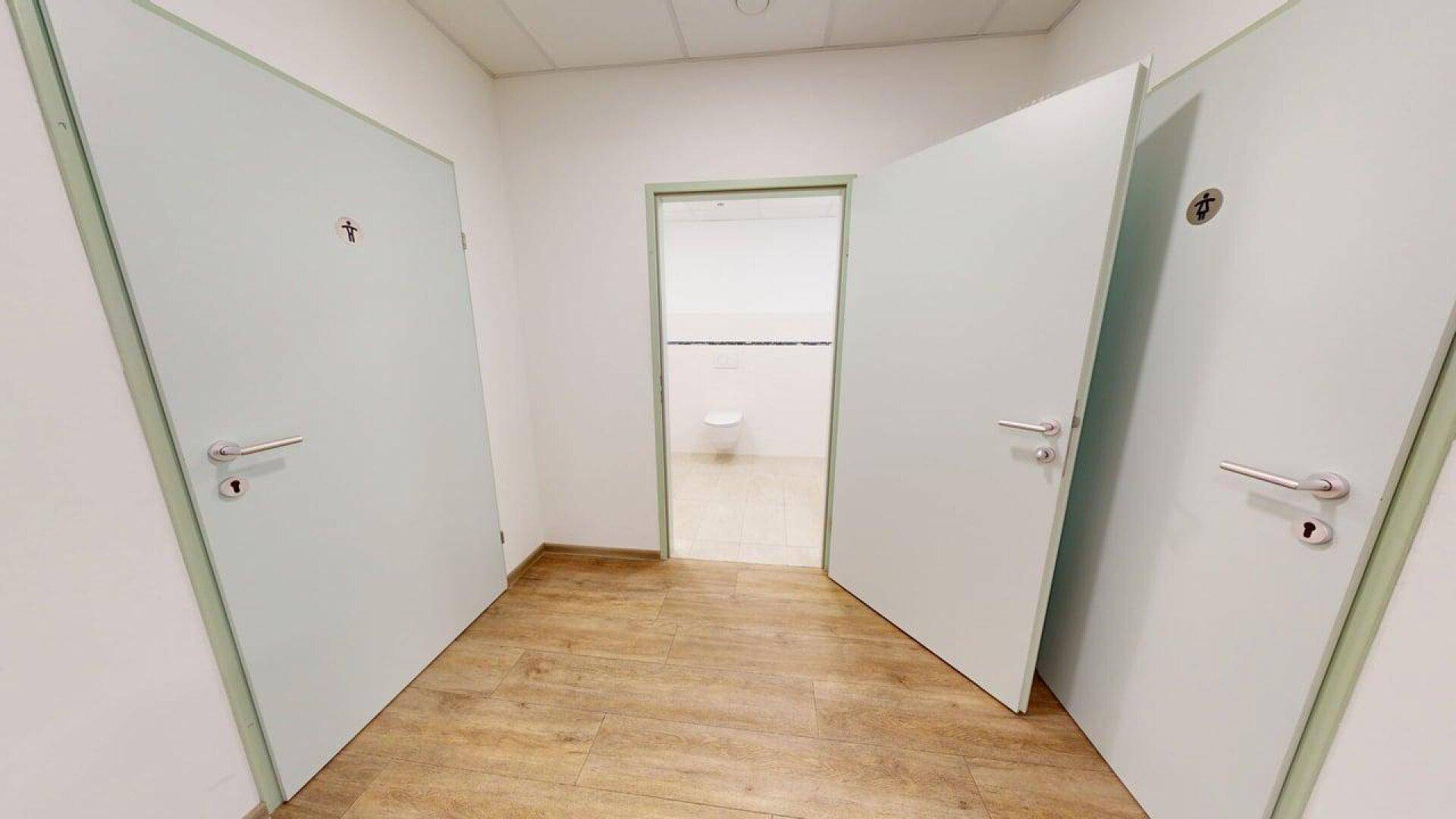 Eingangsbereich zu mehreren Toilettenräumen mit Holzboden und hellen Türen, sauber und funktional.