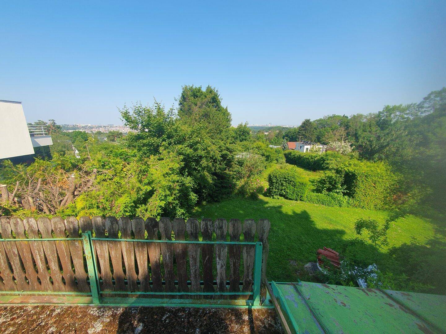 Grüner Gartenbereich mit Rasenfläche, Bäumen und Blick auf die Stadt in der Ferne.