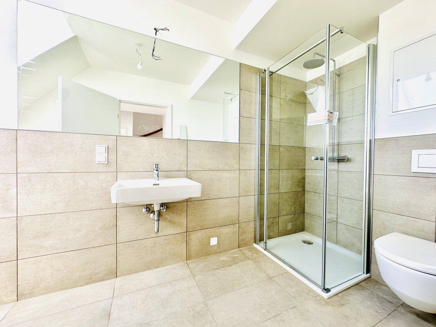 Modernes Badezimmer mit großem Spiegel, ebenerdiger Dusche und Wand-WC.