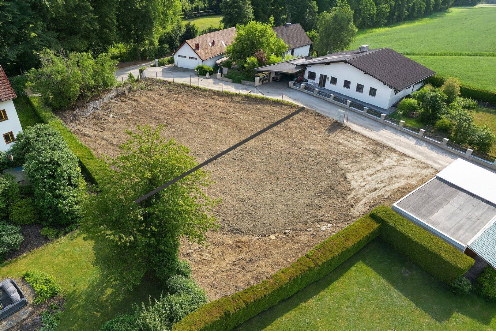 Übersicht aus der Vogelperspektive auf ein großes Baugrundstück umgeben von bestehenden Wohnhäusern und Feldern.