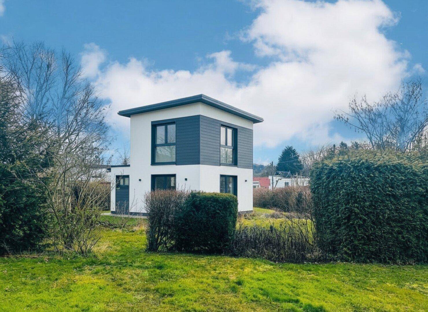 Modernes Einfamilienhaus mit weißer Fassade und dunklen Akzenten, umgeben von einem grünen Garten.