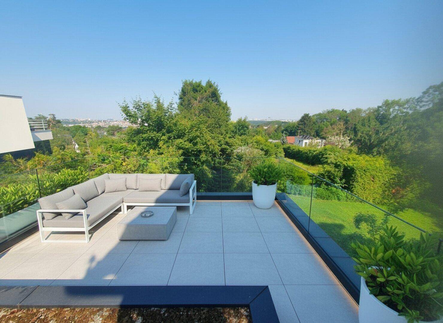 Moderne Dachterrasse mit bequemen Lounge-Möbeln, Glasgeländer und weitem Blick ins Grüne und die Ferne.