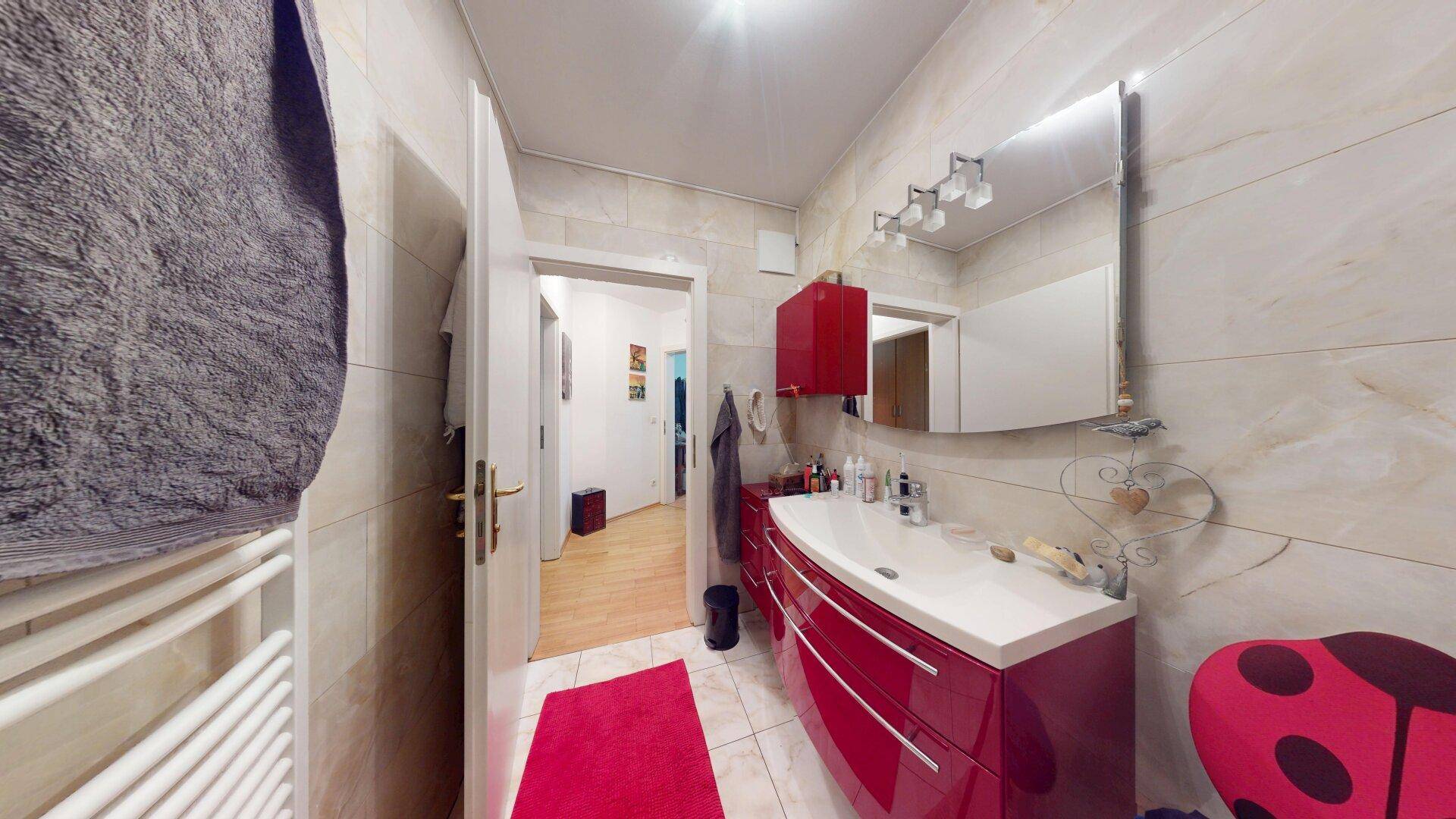 Badezimmer mit rotem Waschtischunterschrank, Spiegel und Zugang zum Flur.