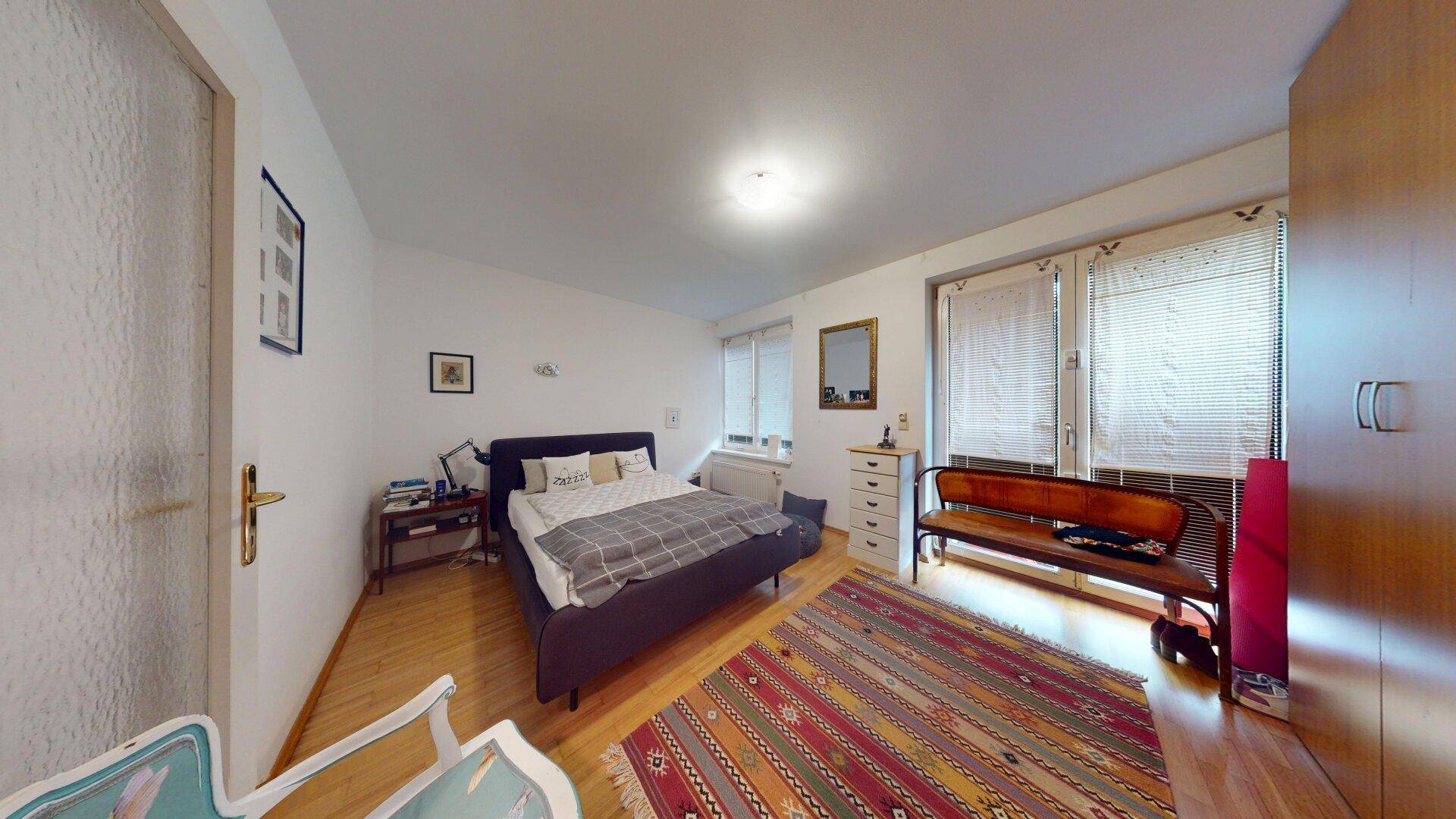 Schlafzimmer mit Doppelbett, Parkettboden und Zugang zur Terrasse.