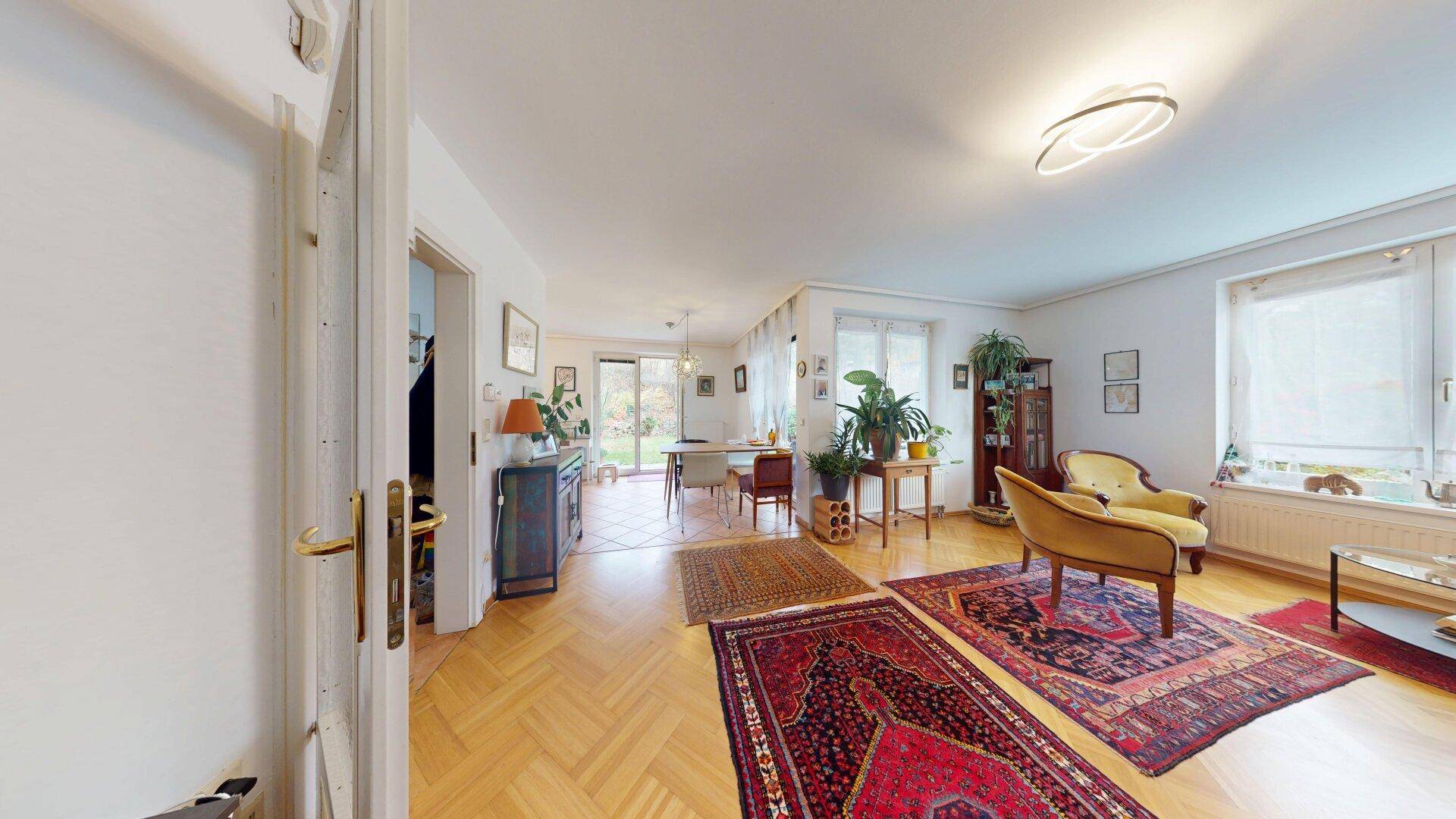 Offener Wohn- und Essbereich mit Parkettboden, Teppichen und Blick in den Garten.