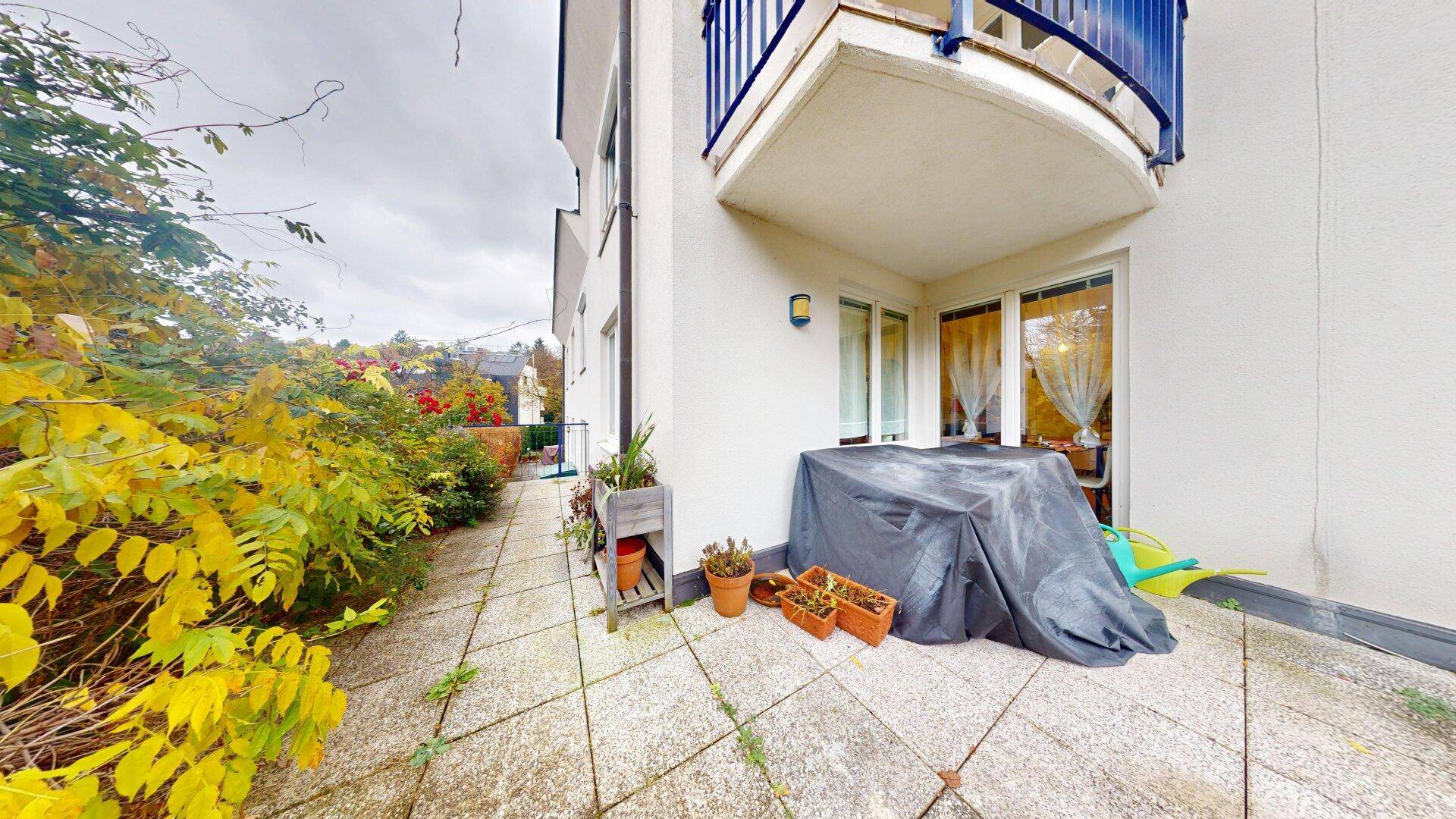 Seitliche Terrasse mit Steinplatten, Pflanzenkübeln und Zugang zum Garten.