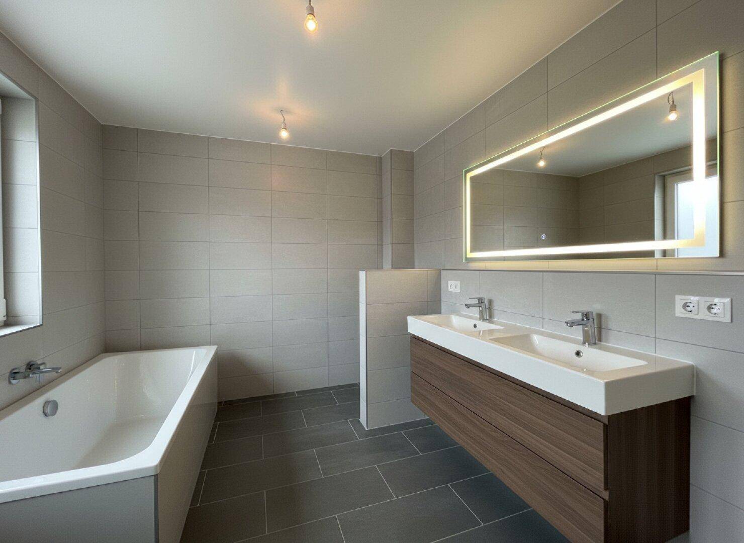 Modernes Badezimmer mit Badewanne, Doppelwaschbecken und beleuchtetem Spiegel.