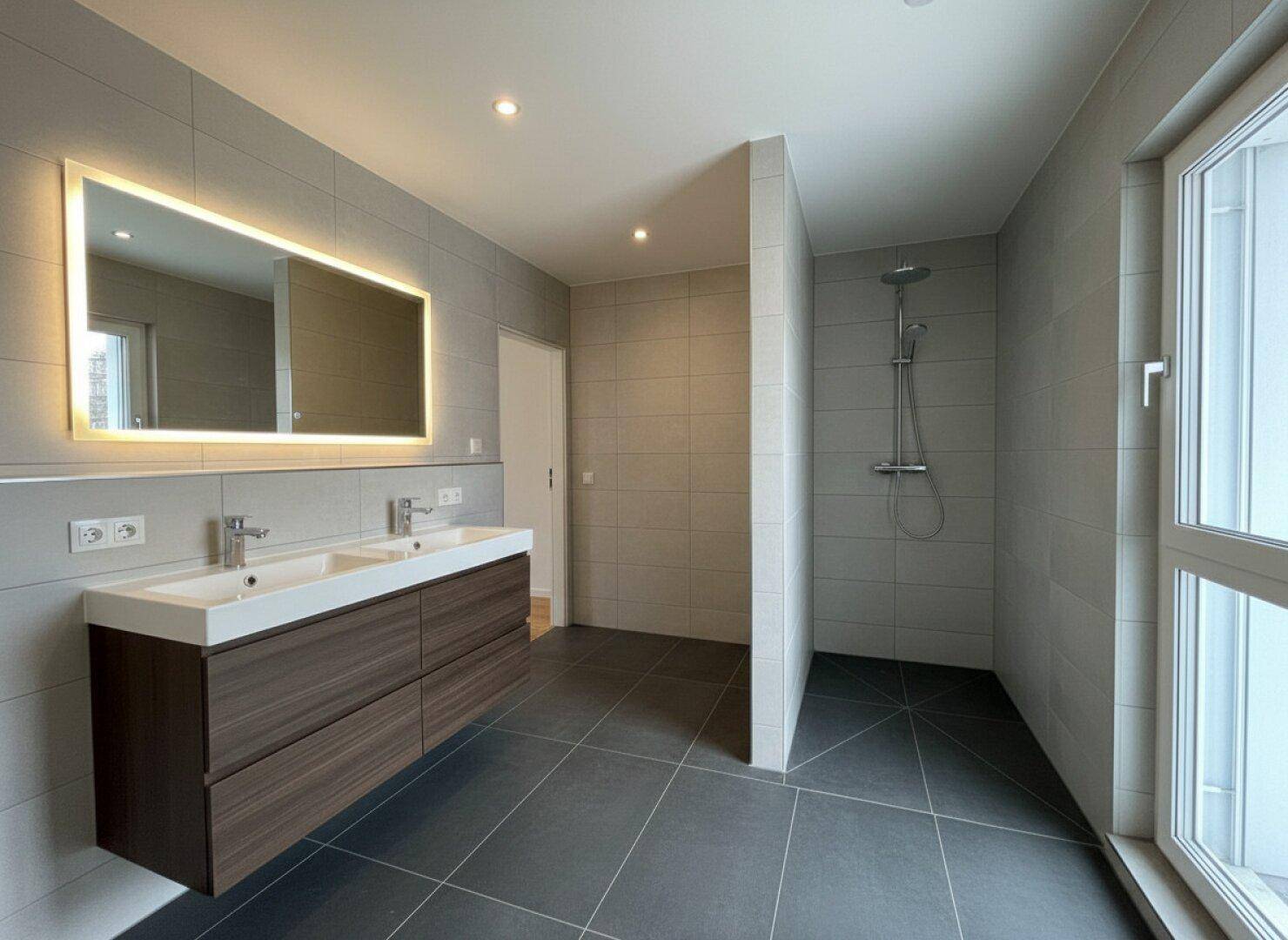 Modernes Badezimmer mit Doppelwaschbecken, großer begehbarer Dusche und grauen Fliesen.