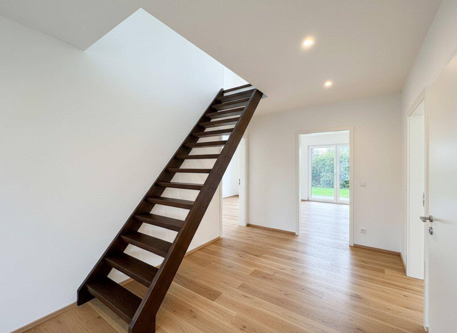 Heller Flur mit moderner Holztreppe, weiß gestrichenen Wänden und Holzboden.