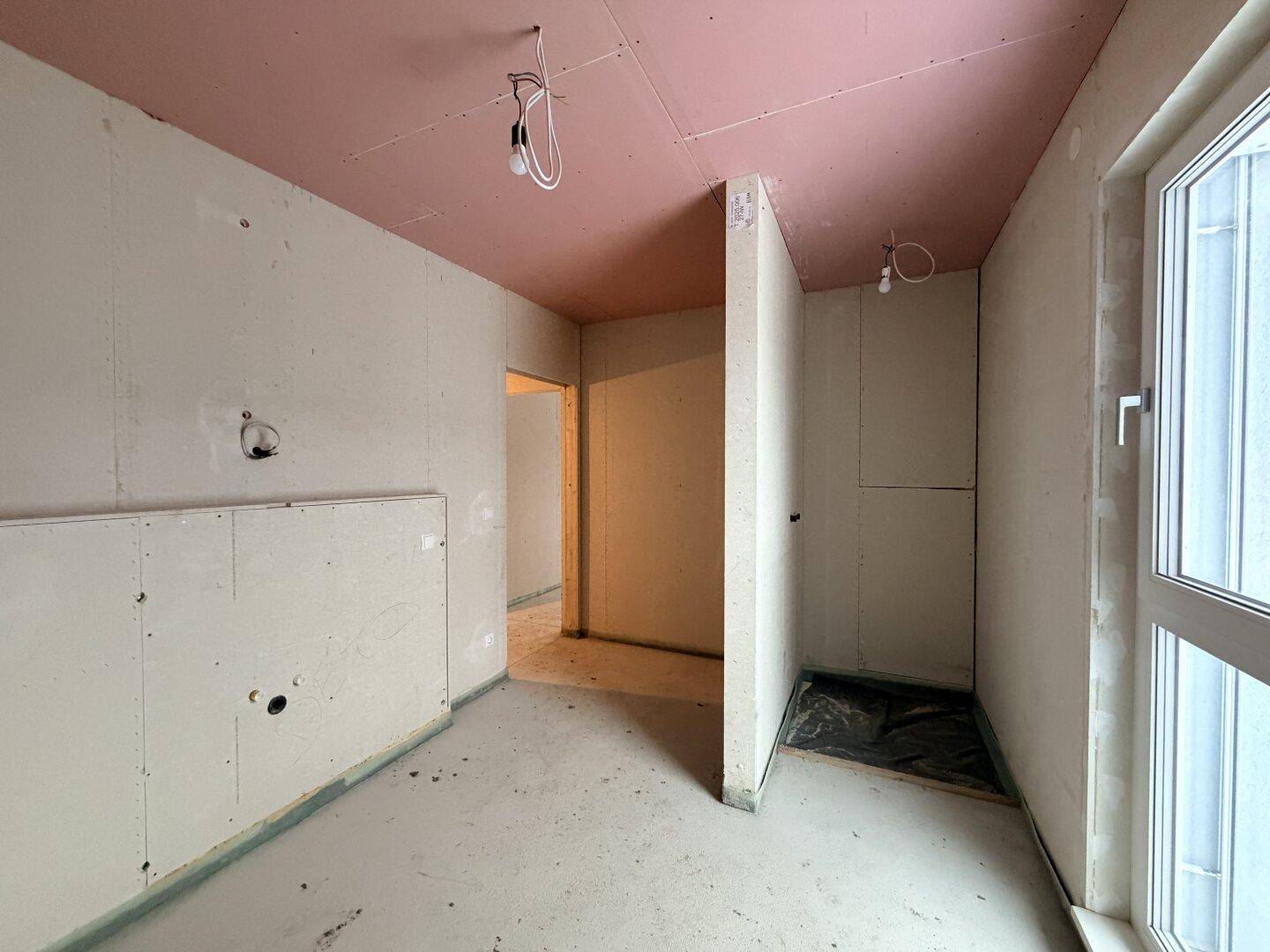 Unfertiges Badezimmer im Rohbau mit Fenster und vorbereiteten Sanitäranschlüssen.