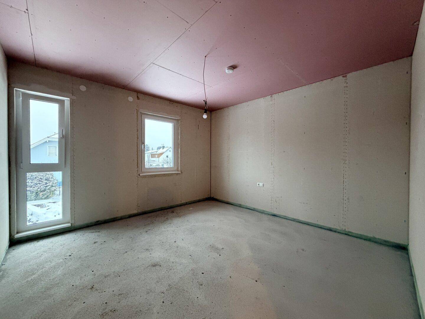 Unfertiges Schlafzimmer im Rohbau mit zwei Fenstern und rosa Decke.