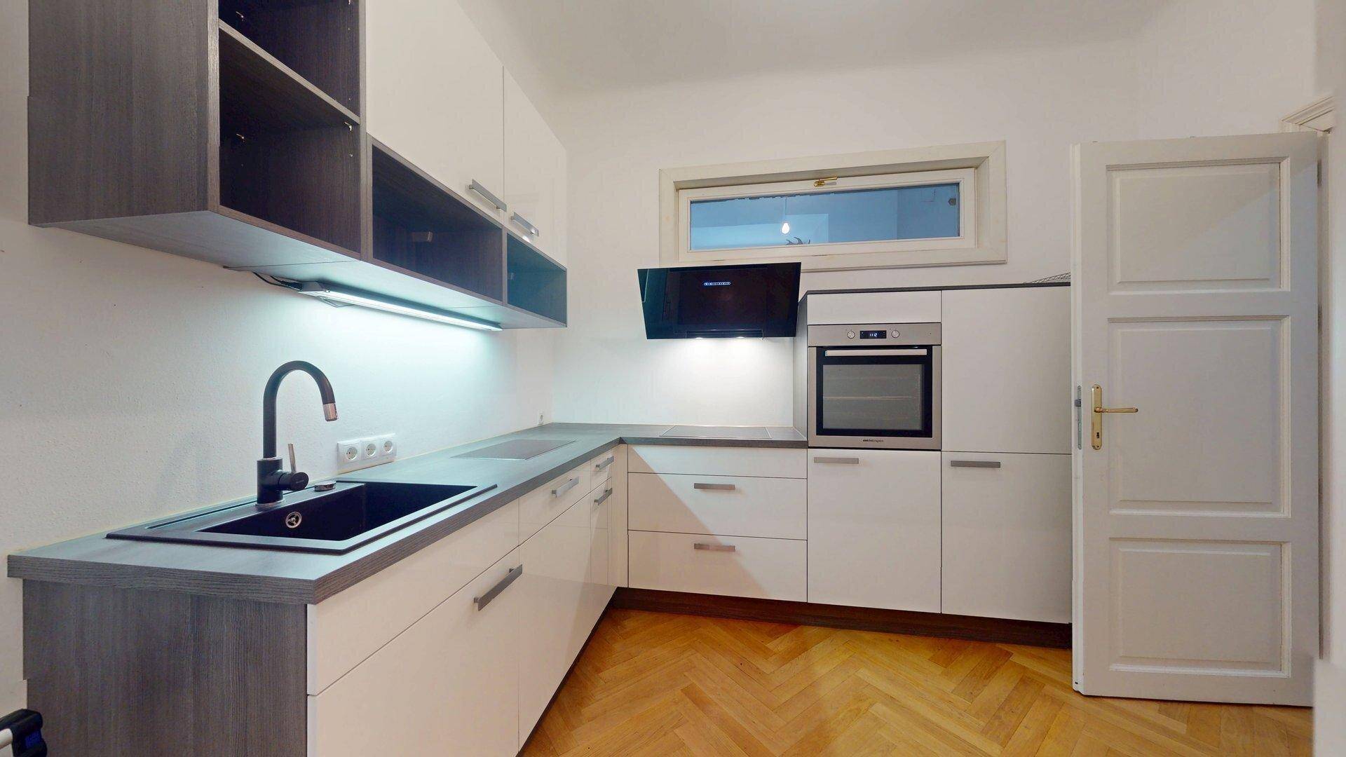 Helle Küche mit weiß-grauen Fronten, Spülbecken und Fenster für natürliches Licht.