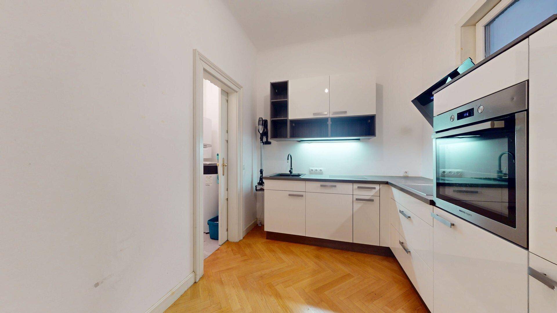 Moderne Küche mit weißen Hochglanzschränken, integriertem Backofen und praktischem Fischgrätparkett.