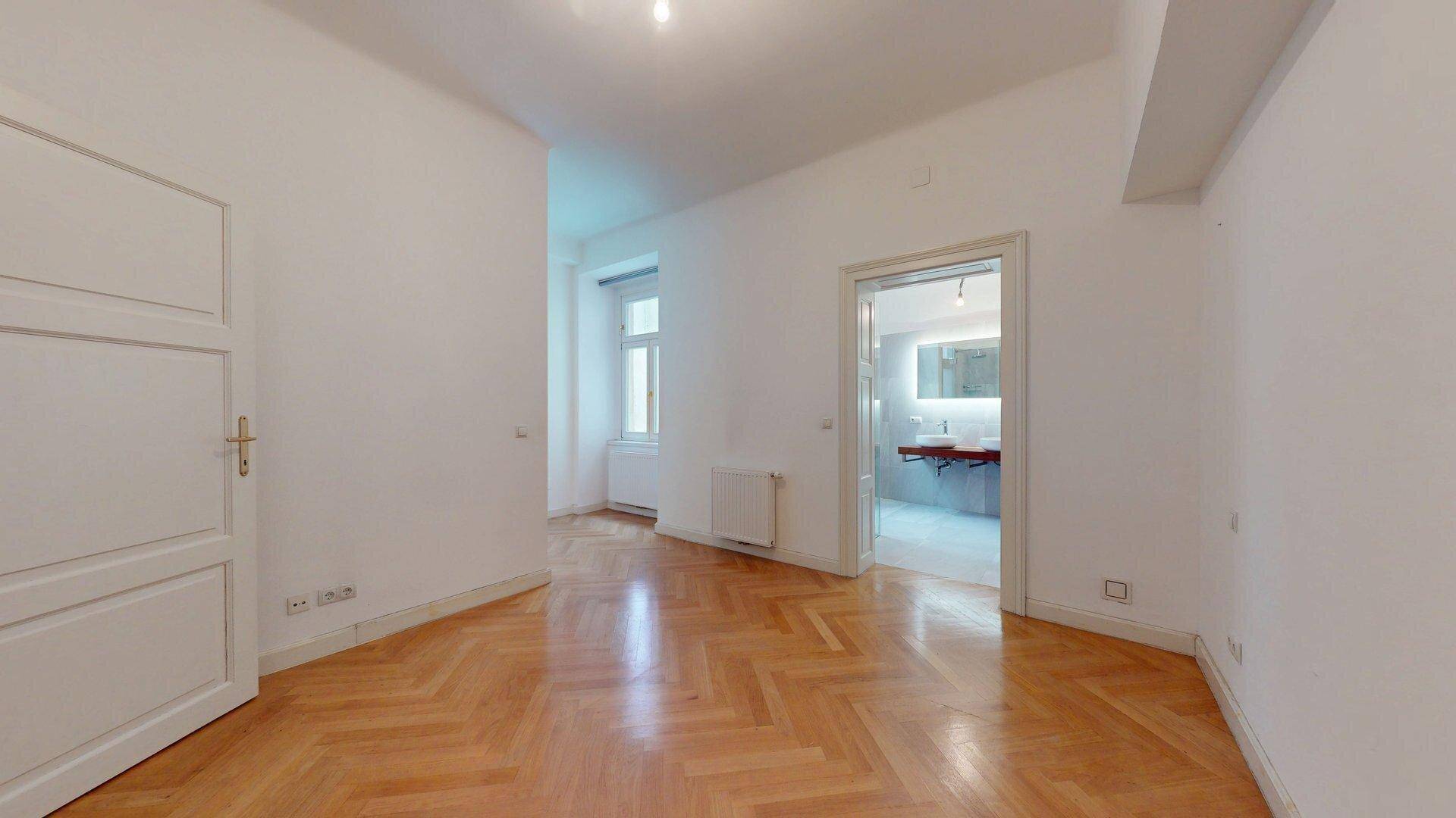 Leerer Raum mit Fischgrätparkett und direktem Zugang zu einem modernen Badezimmer.