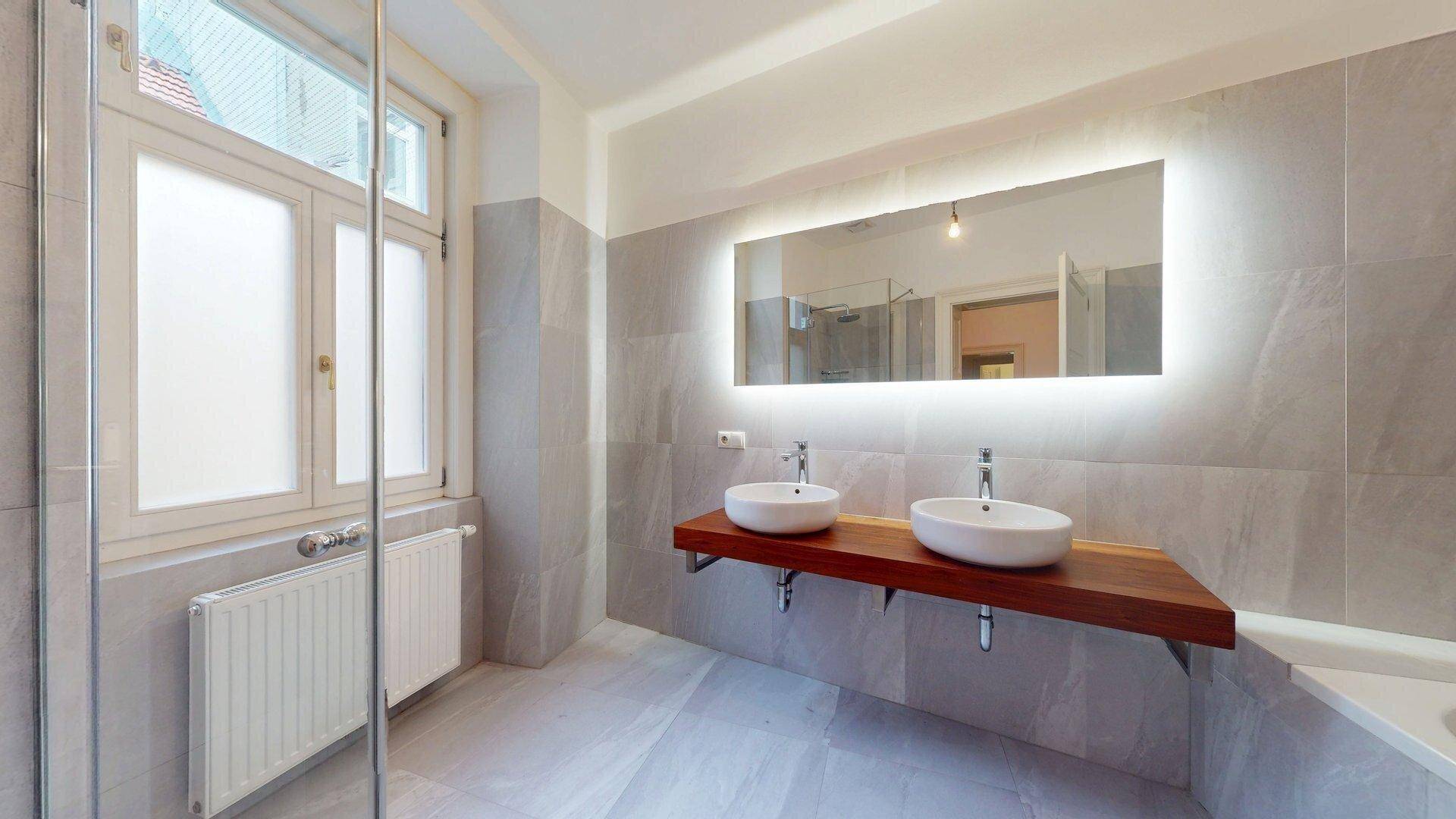 Modernes Badezimmer mit doppelten Waschbecken, großem beleuchtetem Spiegel und Fenster.