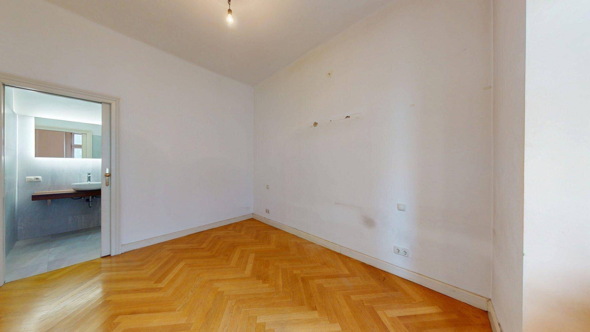 Leerer Raum mit Fischgrätparkett und direktem Zugang zu einem modernen Badezimmer.