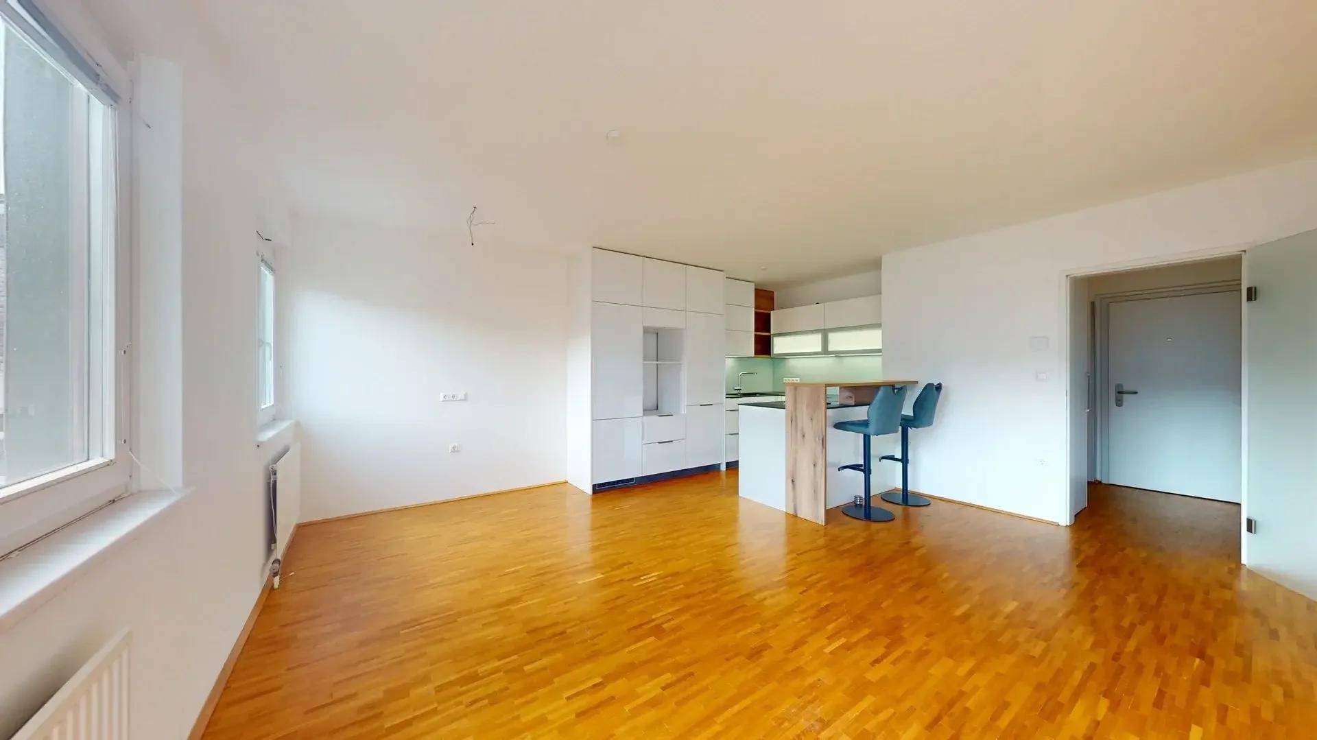 Geräumiger offener Wohnbereich mit Holzboden, viel Tageslicht und einer modernen Küchenzeile mit Barhockern.