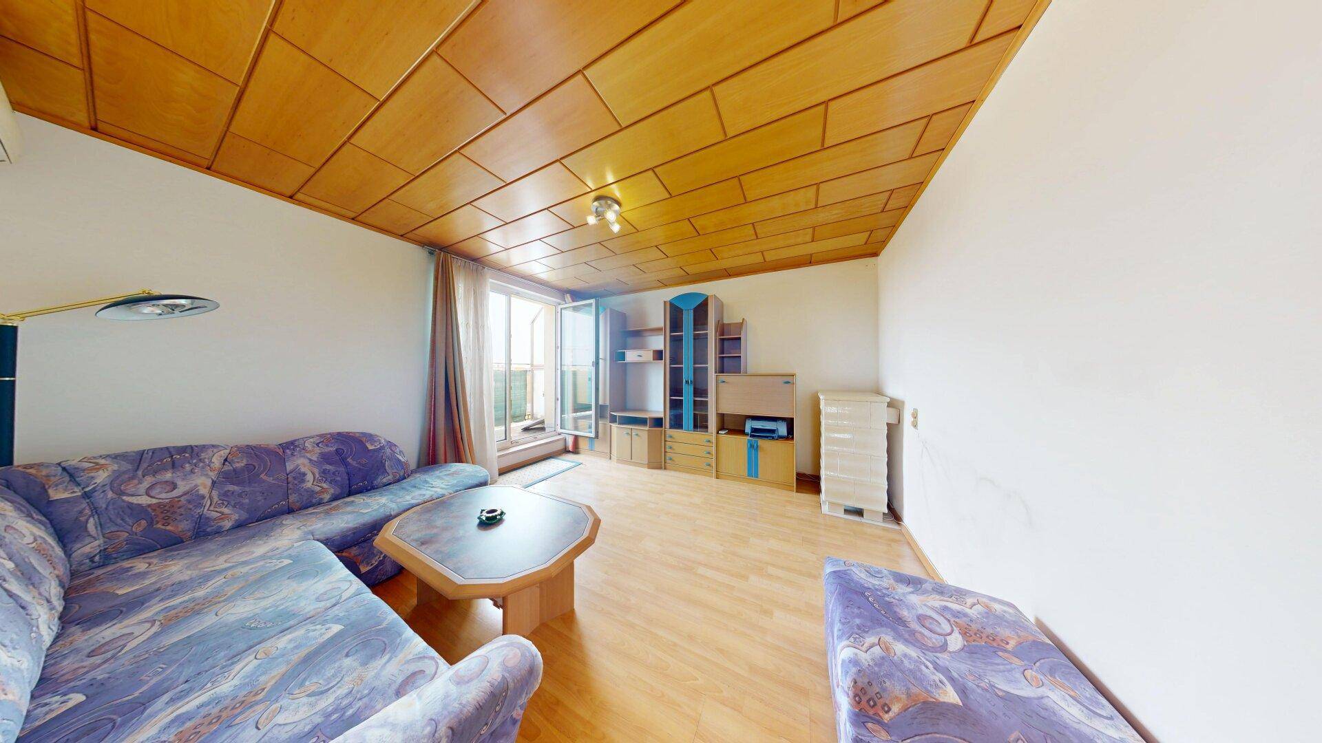 Gemütliches Wohnzimmer mit Holzdecke, Parkettboden und Zugang zu einem Balkon.