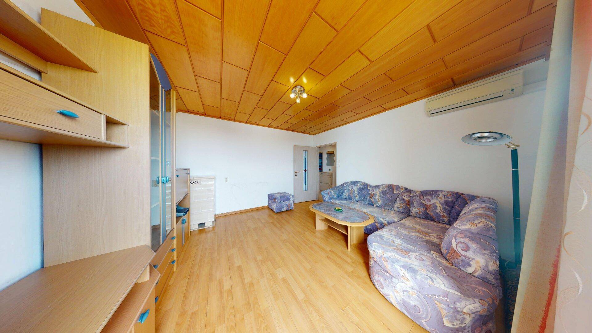 Wohnzimmer mit Holzdecke, Parkettboden und einer Klimaanlage an der Wand.