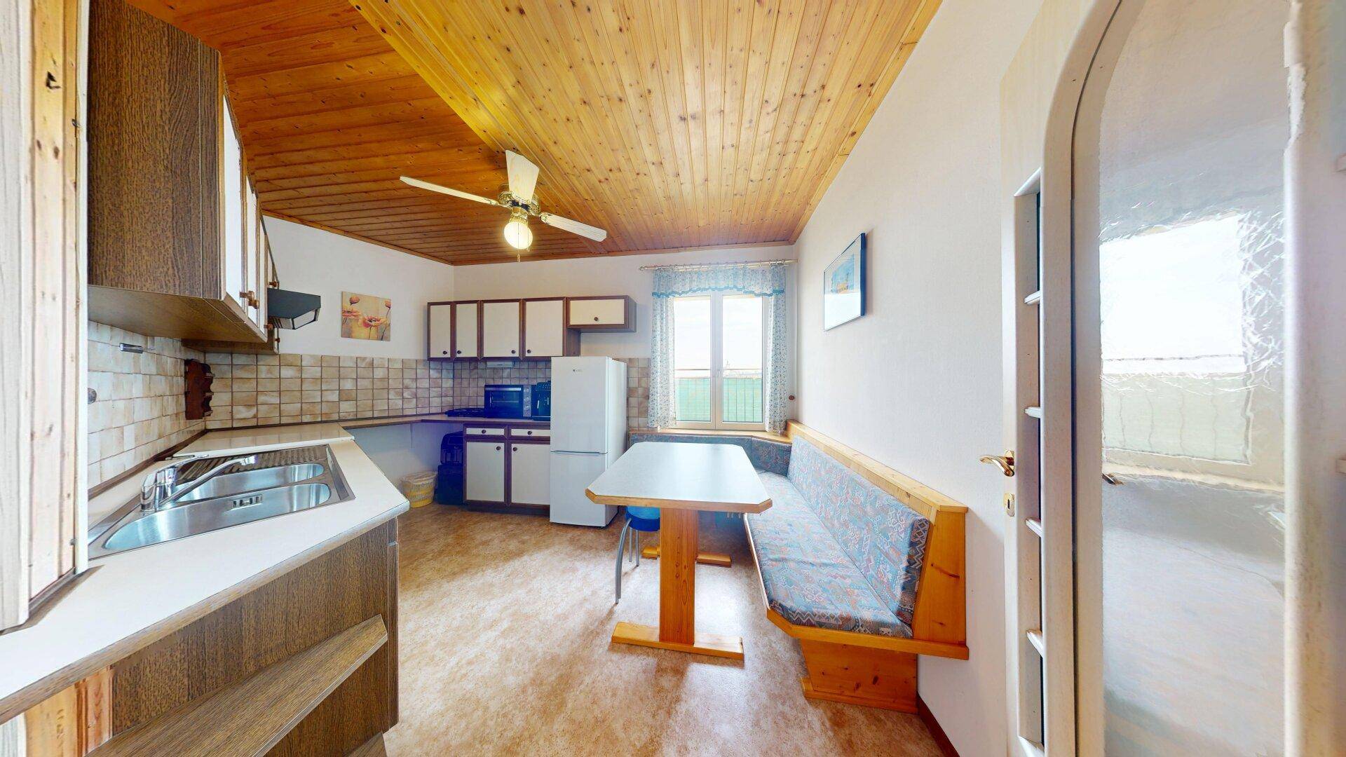 Funktionale Küche mit Holzdecke, Essbereich und Fliesenboden.
