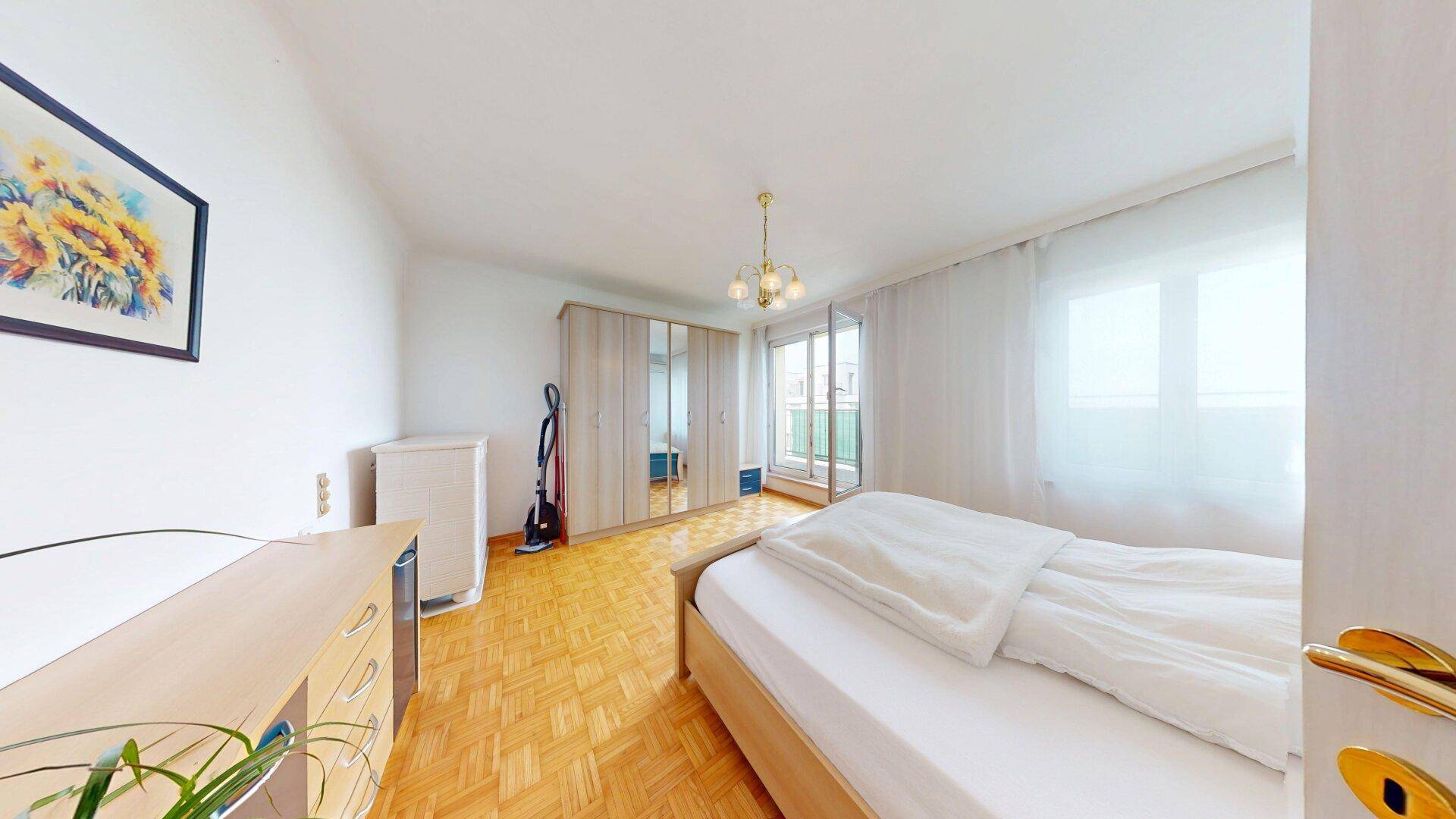 Helles Schlafzimmer mit Parkettboden, großem Kleiderschrank und Zugang zu einem Balkon.