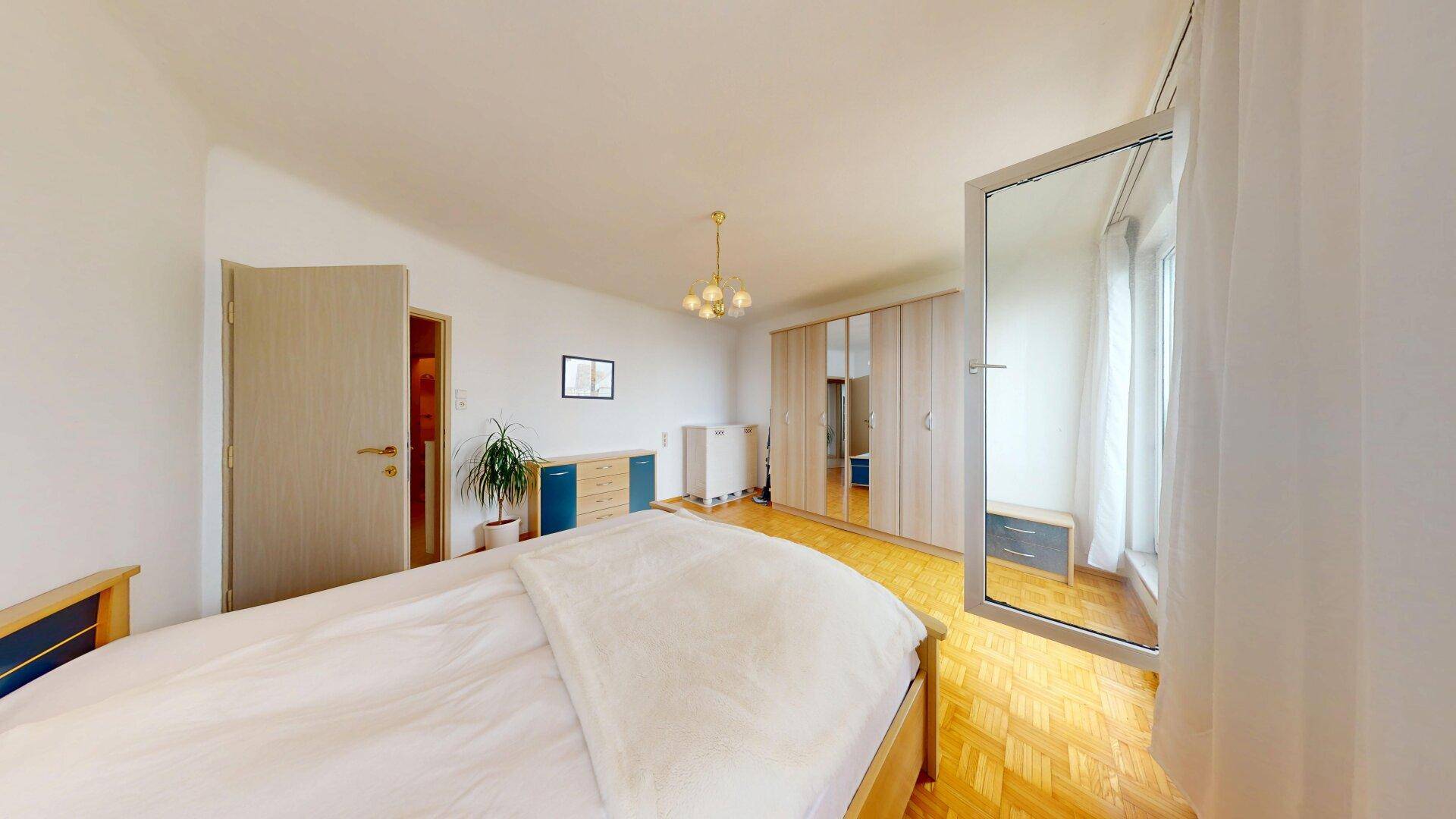 Schlafzimmer mit Parkettboden, großem Spiegel und hellem Ambiente.
