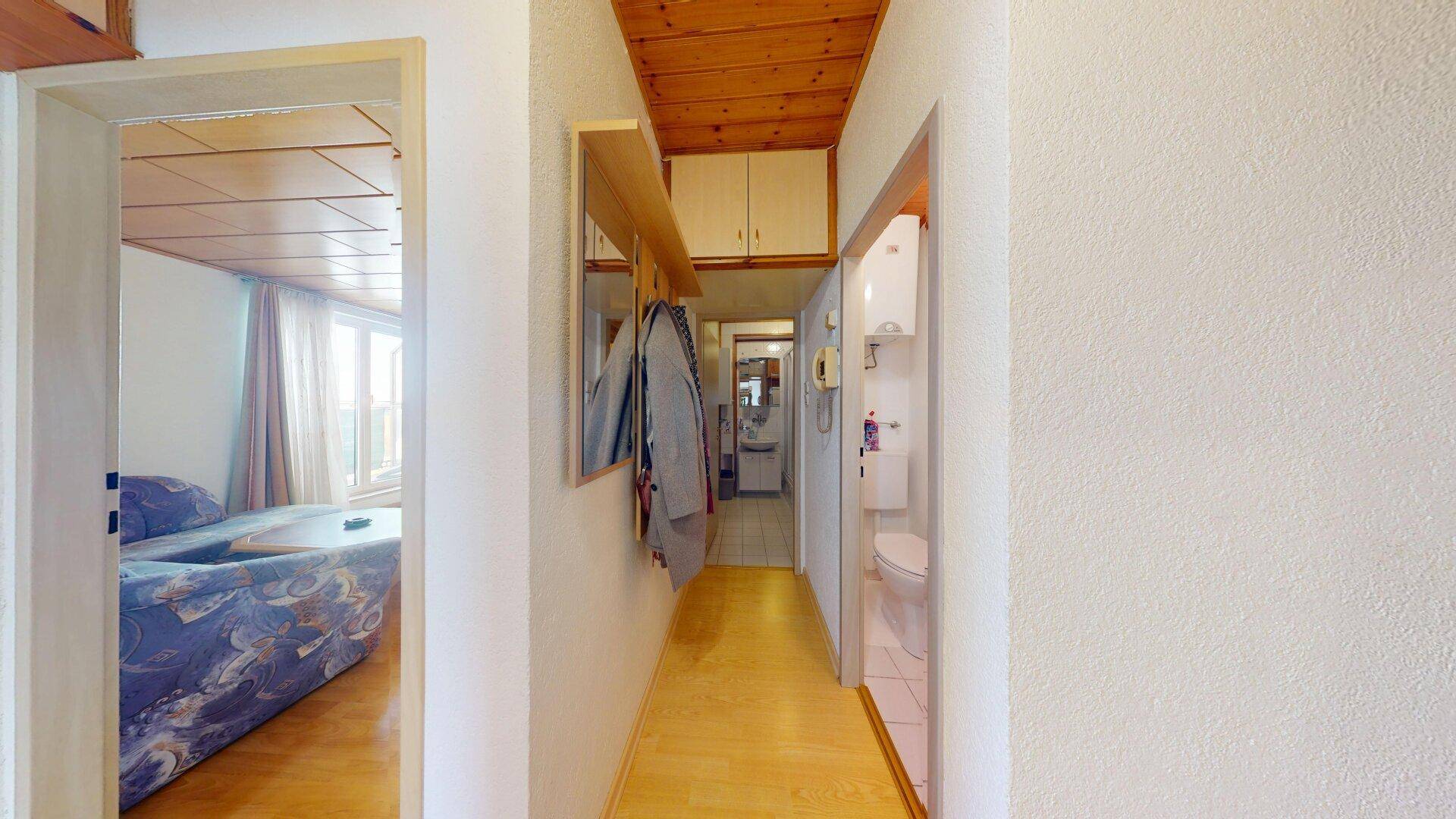 Langer Flur mit Holzdecke, Garderobe und Zugang zu Bad und WC.