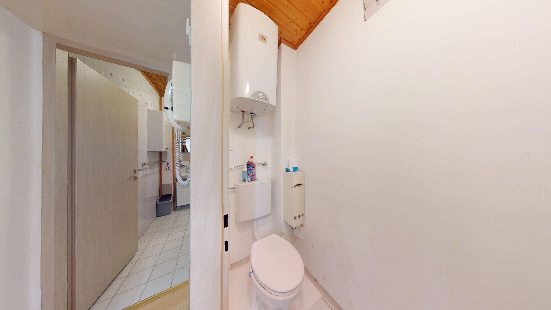 Separates WC mit Toilette und Warmwasserboiler an der Wand.