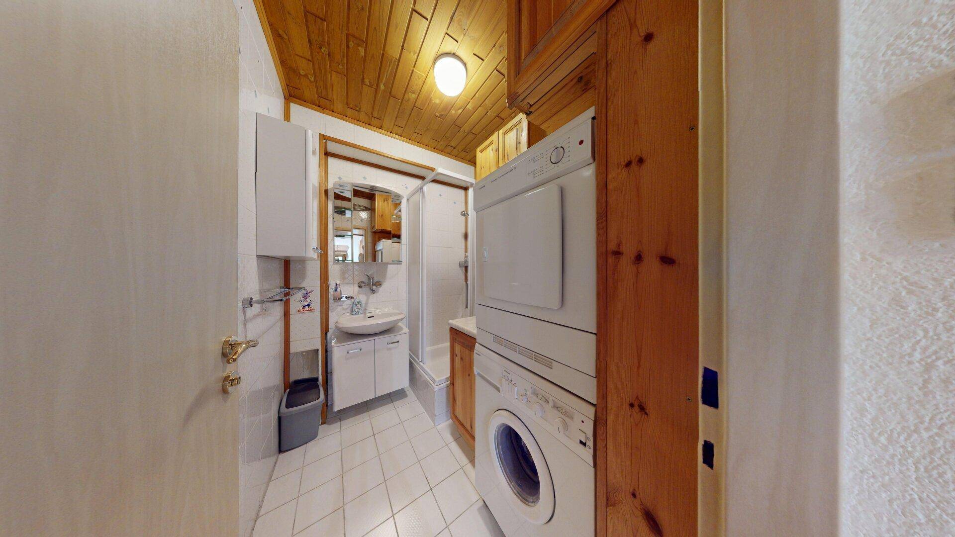 Badezimmer mit Holzdecke, Fliesenboden, Waschmaschine und Trockner.