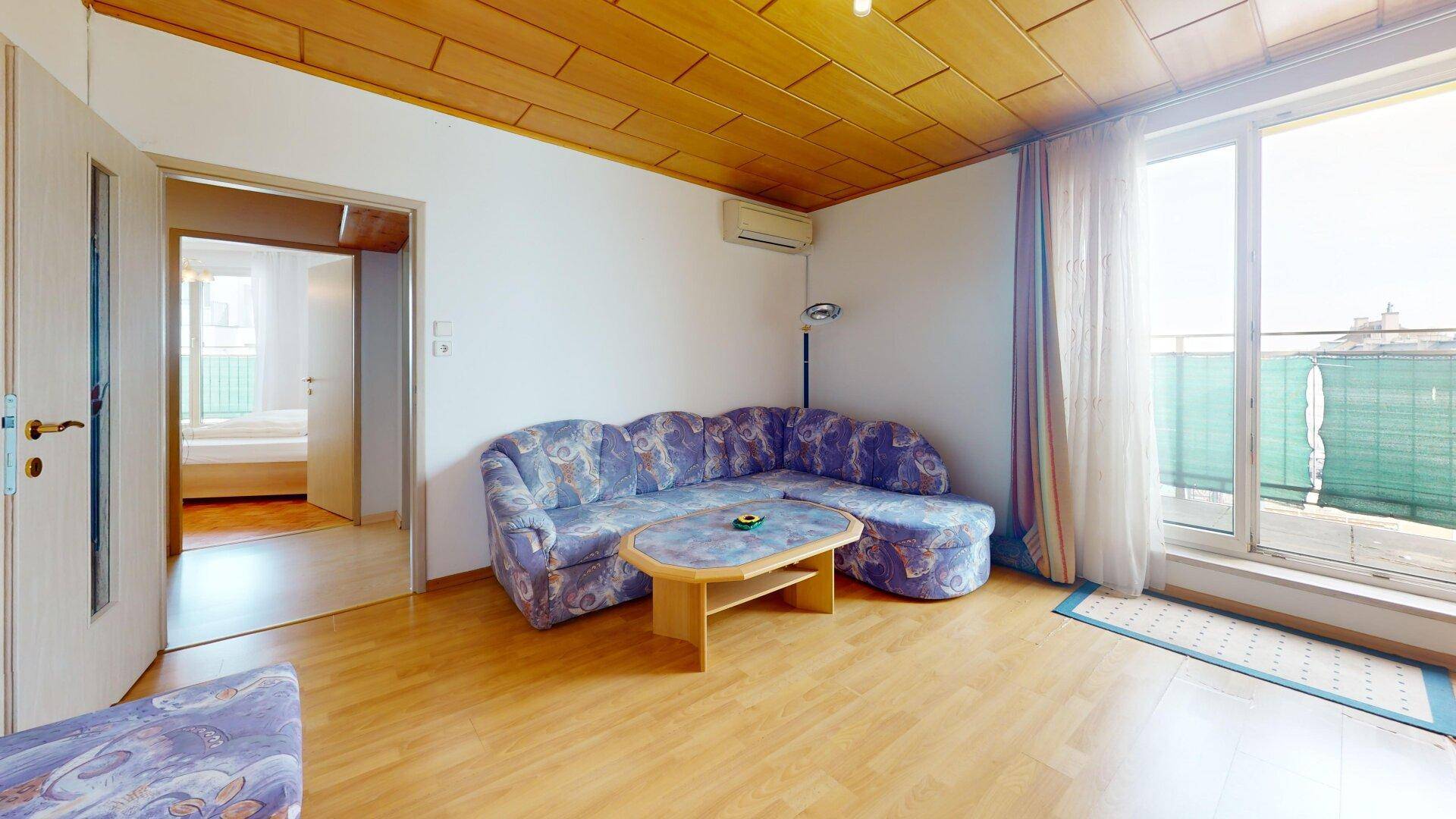 Wohnzimmer mit Holzdecke, Parkettboden und Zugang zu einem Balkon mit Stadtblick.
