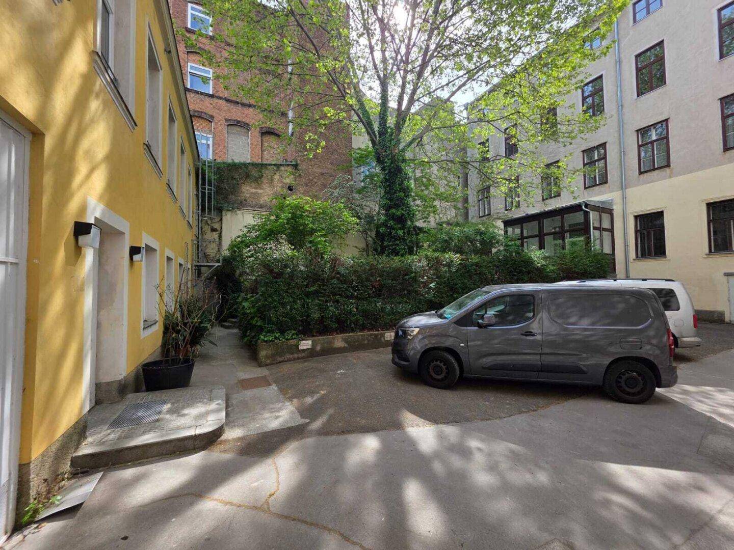 Innenhof mit geparkten Fahrzeugen, umgeben von Gebäuden und üppiger Bepflanzung.