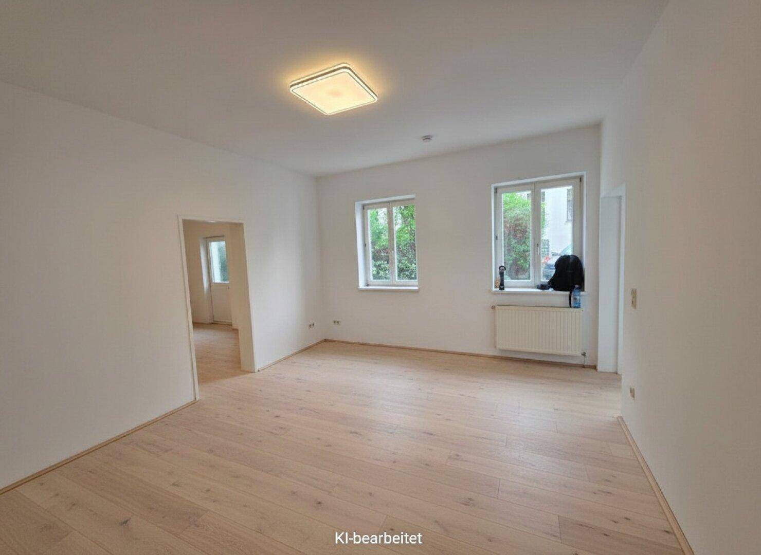 Geräumiger, heller Raum mit Holzboden und zwei Fenstern, die einen Blick ins Grüne bieten.