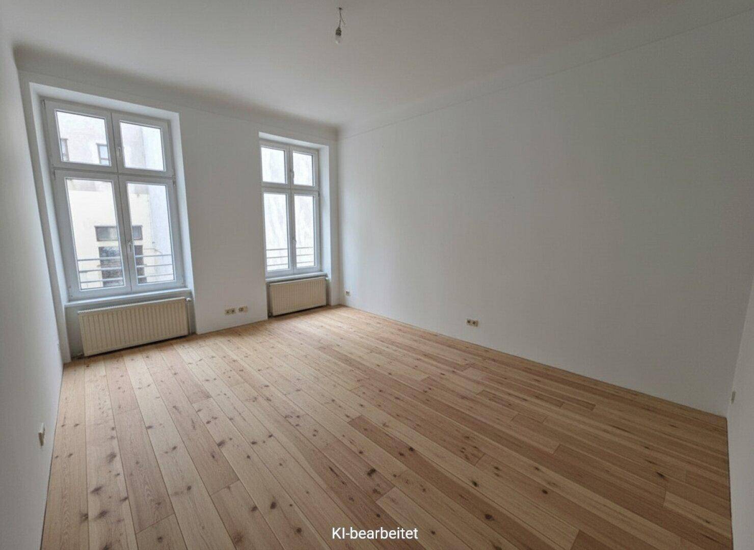 Leerer Raum mit breiten Holzdielen, hohen Fenstern und weiß gestrichenen Wänden, bereit zur Einrichtung.