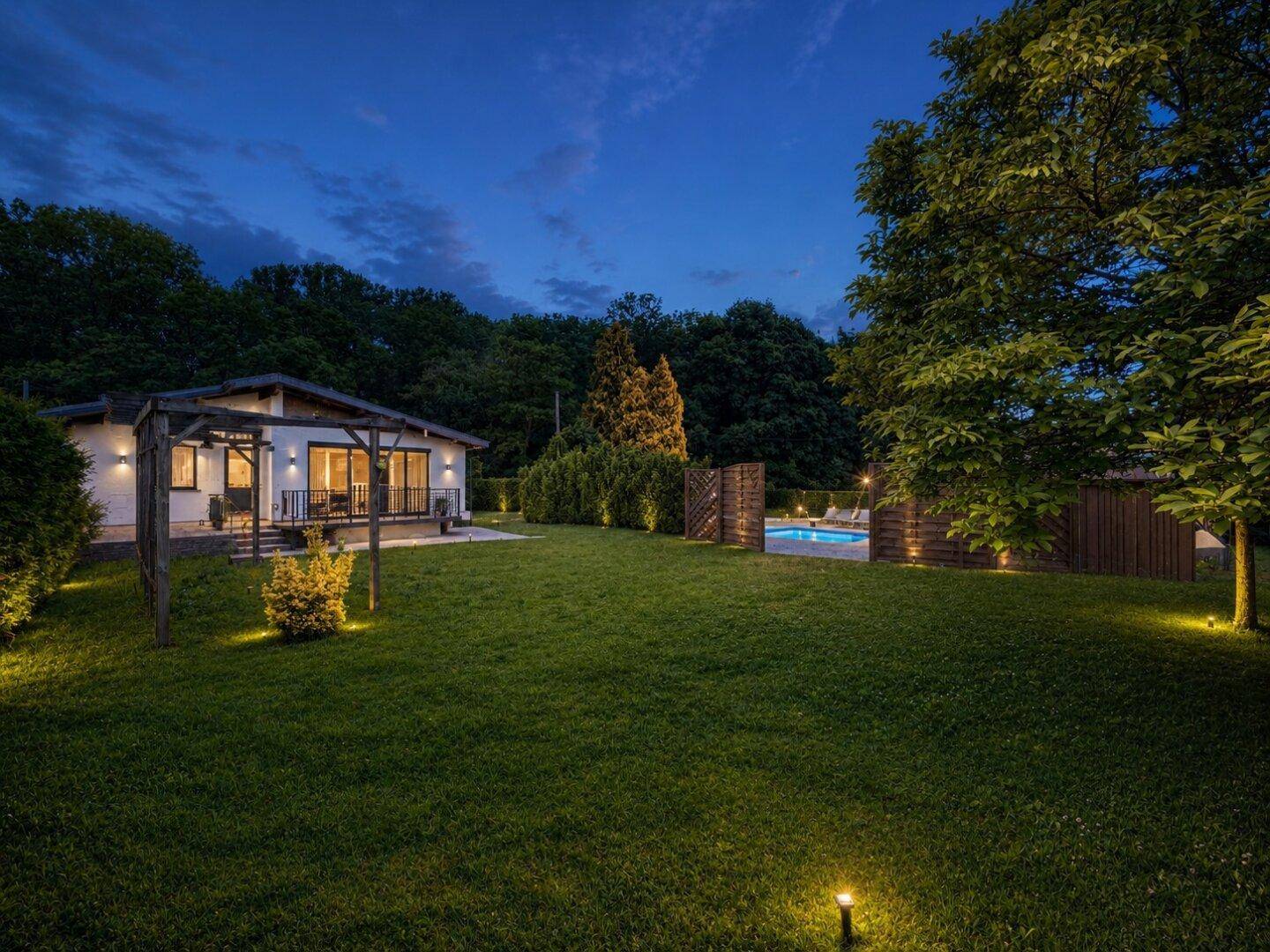 Beleuchteter Garten und renoviertes Haus bei Nacht mit stimmungsvoller Außenbeleuchtung.