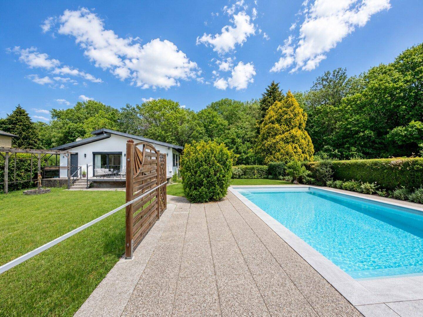 Renoviertes Haus mit gepflastertem Weg, offenem Swimmingpool und gepflegter Gartenanlage.
