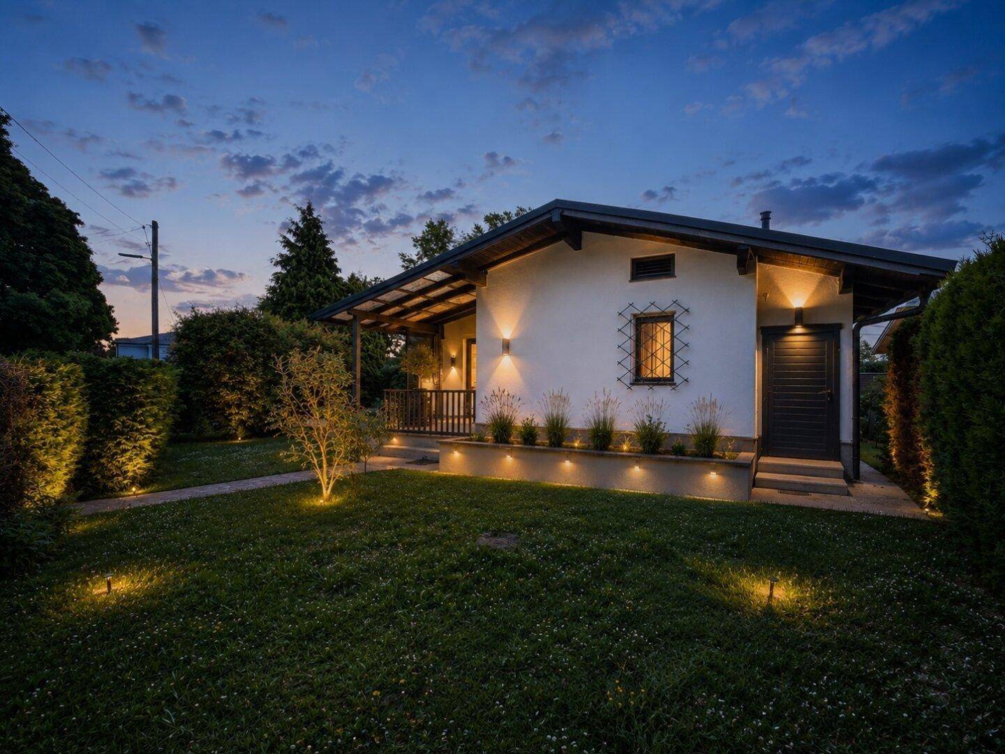 Beleuchtete Seitenansicht des renovierten Hauses bei Nacht mit akzentuierter Gartenbeleuchtung.
