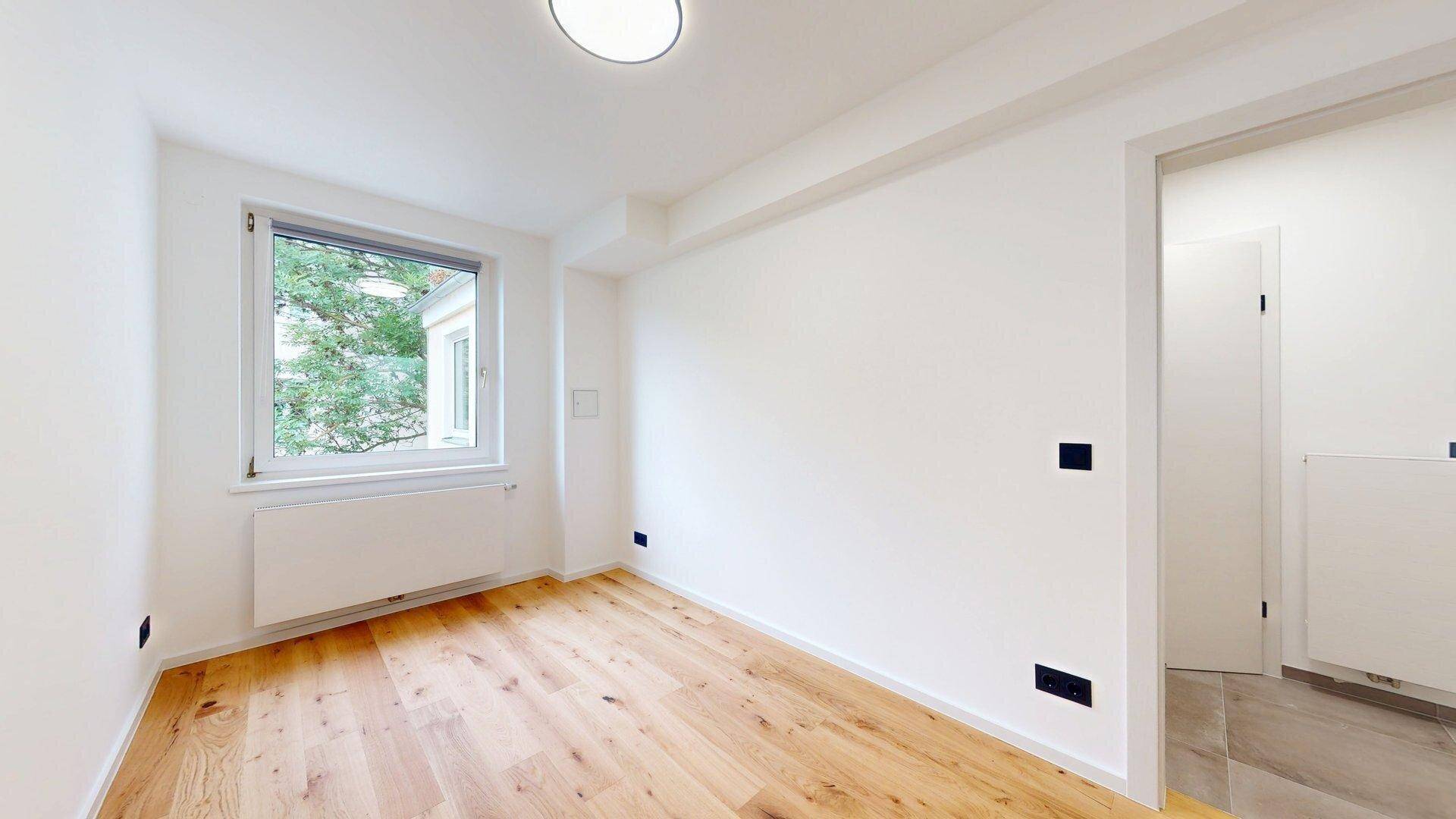 Gemütliches Schlafzimmer mit Holzboden und Fenster, das viel natürliches Licht hereinlässt.