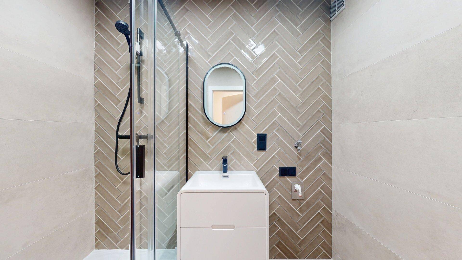 Elegantes Badezimmer mit begehbarer Dusche, modernem Waschtisch und Fliesen im Fischgrätmuster.