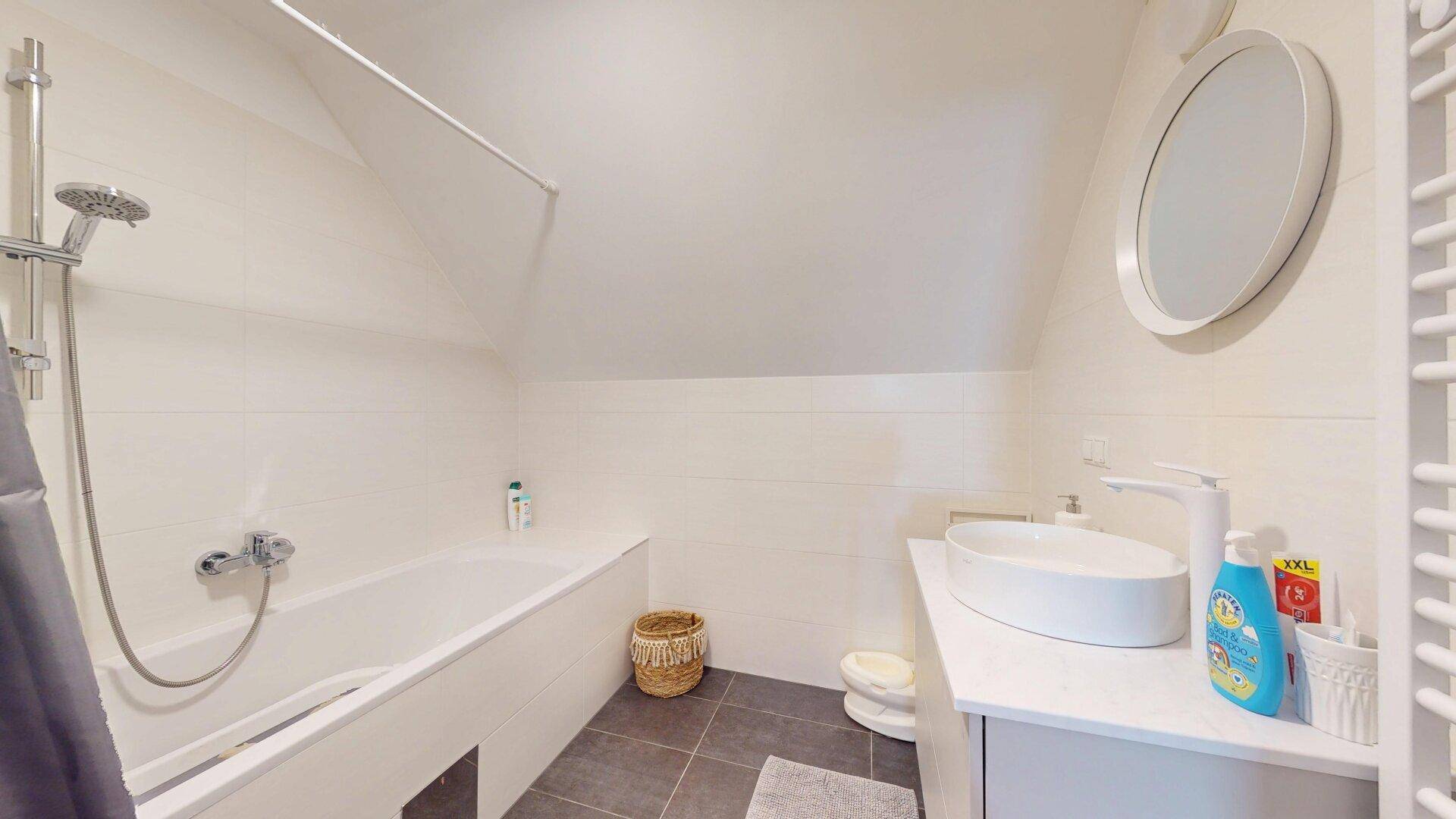 Modernes Badezimmer mit Badewanne, Waschbecken und beheiztem Handtuchhalter unter Dachschräge.