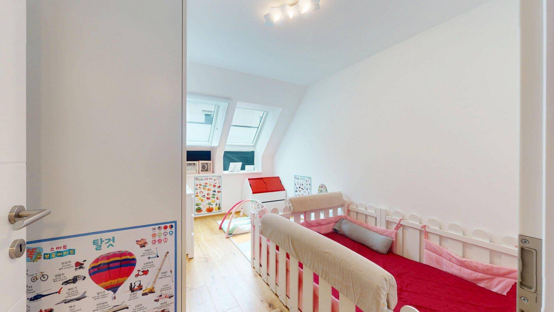 Kinderzimmer mit Babybett, Spielbereich und Dachfenstern für viel Tageslicht.