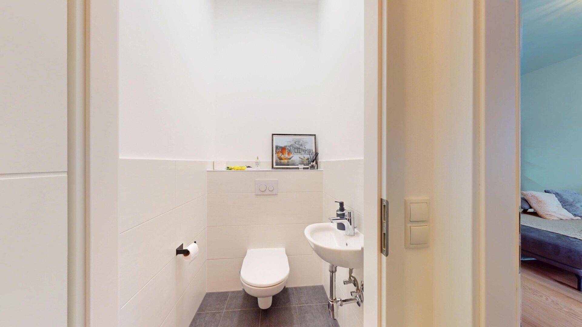 Modernes Gäste-WC mit Wand-WC und kleinem Waschbecken, ausgestattet mit hellen Fliesen.