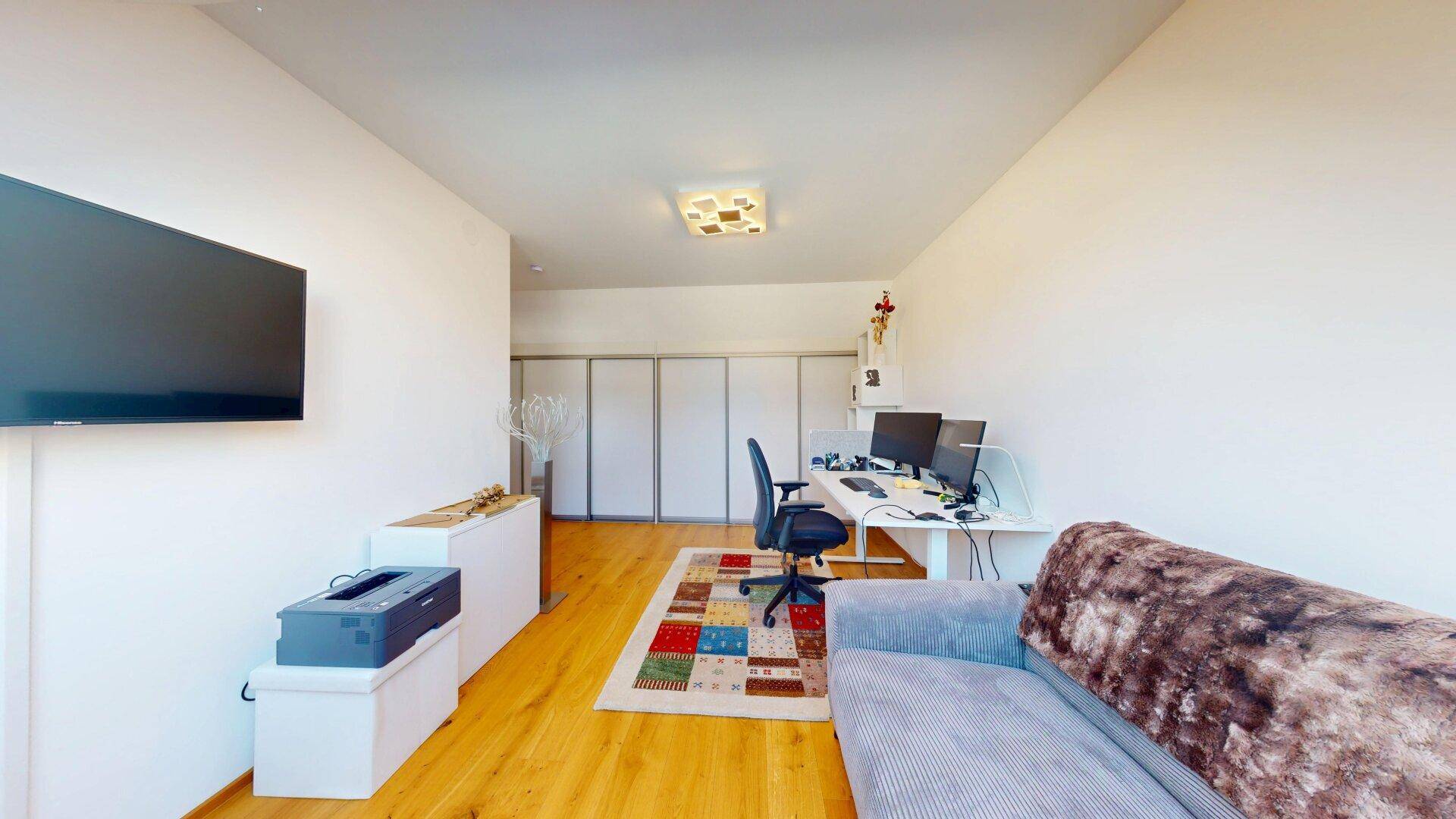 Helles Arbeitszimmer mit Schreibtisch, Computern und einem Sofa, ausgestattet mit Holzboden.
