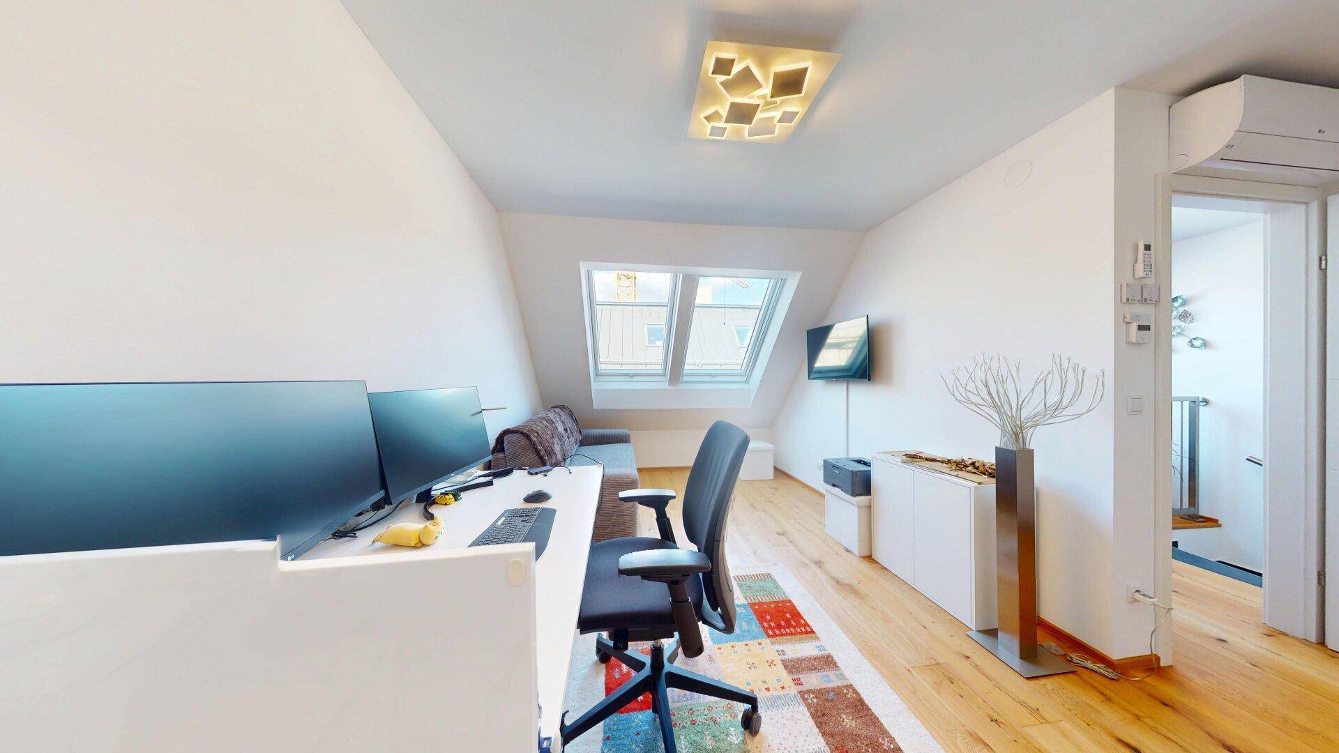 Arbeitsbereich mit Dachfenstern, Schreibtisch und Blick auf die Umgebung.