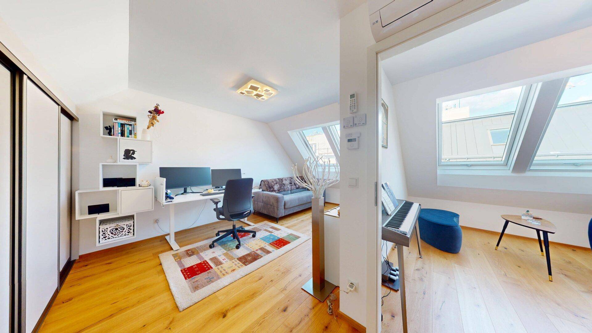 Geräumiges Arbeitszimmer mit Schreibtisch, Schränken und Zugang zu einem weiteren Bereich mit Klavier.