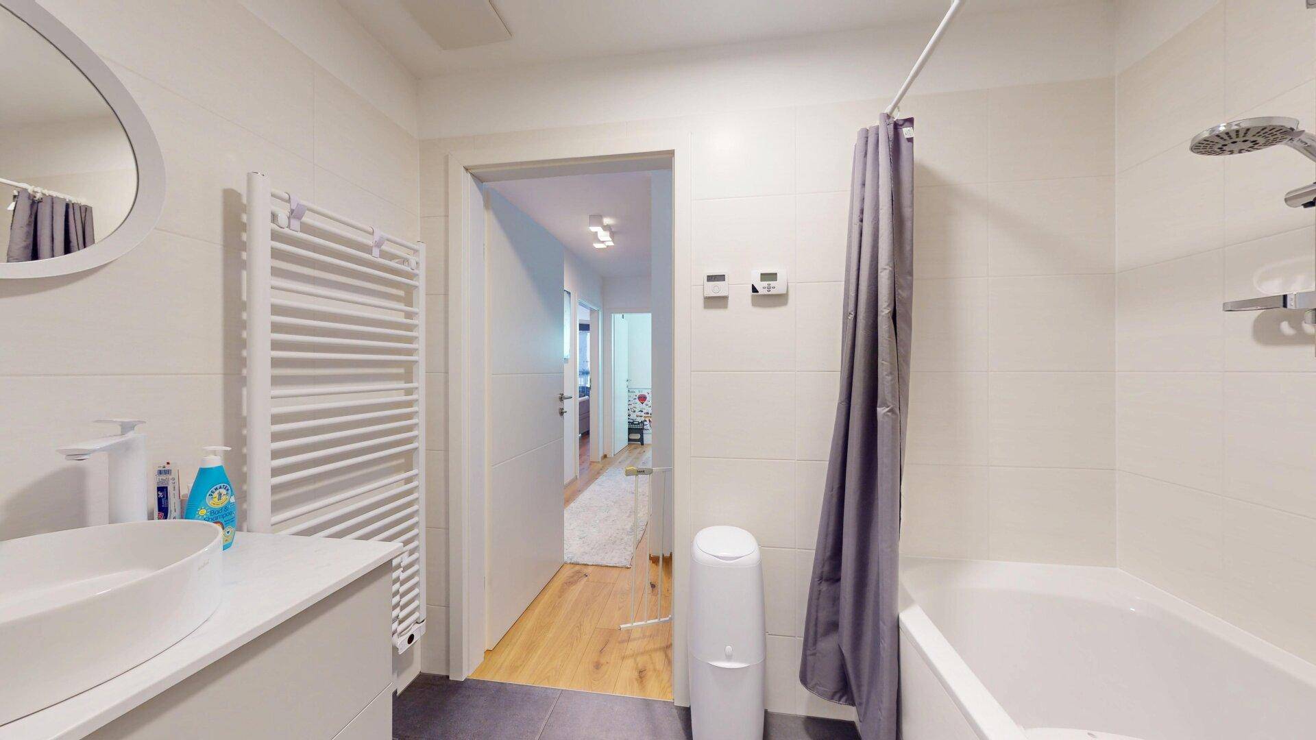Helles Badezimmer mit Badewanne, modernem Waschbecken und Zugang zum Flur.
