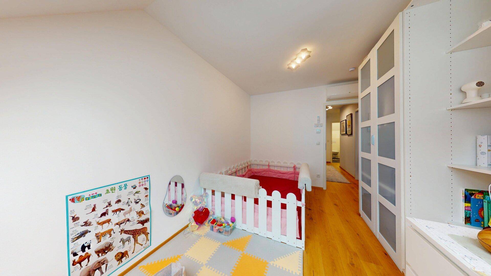 Helles Kinderzimmer mit Spielbereich, Babybett und integrierten Schränken.