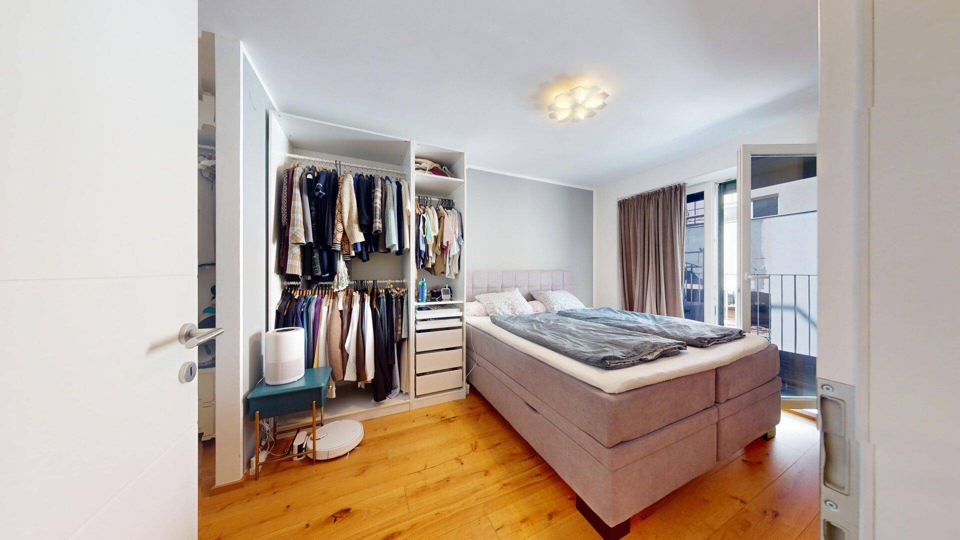 Schlafzimmer mit Doppelbett, offenem Kleiderschrank und Zugang zum Balkon.