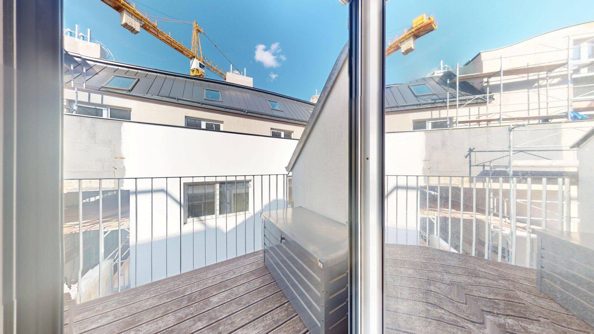 Kleiner Balkon mit Holzboden und Blick auf die umliegenden Gebäude und Baustelle.