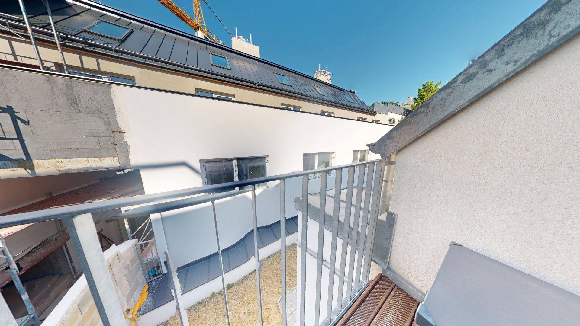 Kleiner Balkon mit Holzboden und Blick auf die umliegenden Gebäude und Baustelle.
